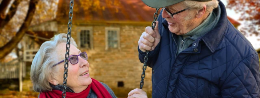 Senior man standing beside senior woman on swing