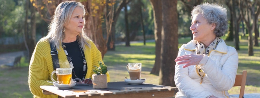 Two older women sitting at the park while having a conversation